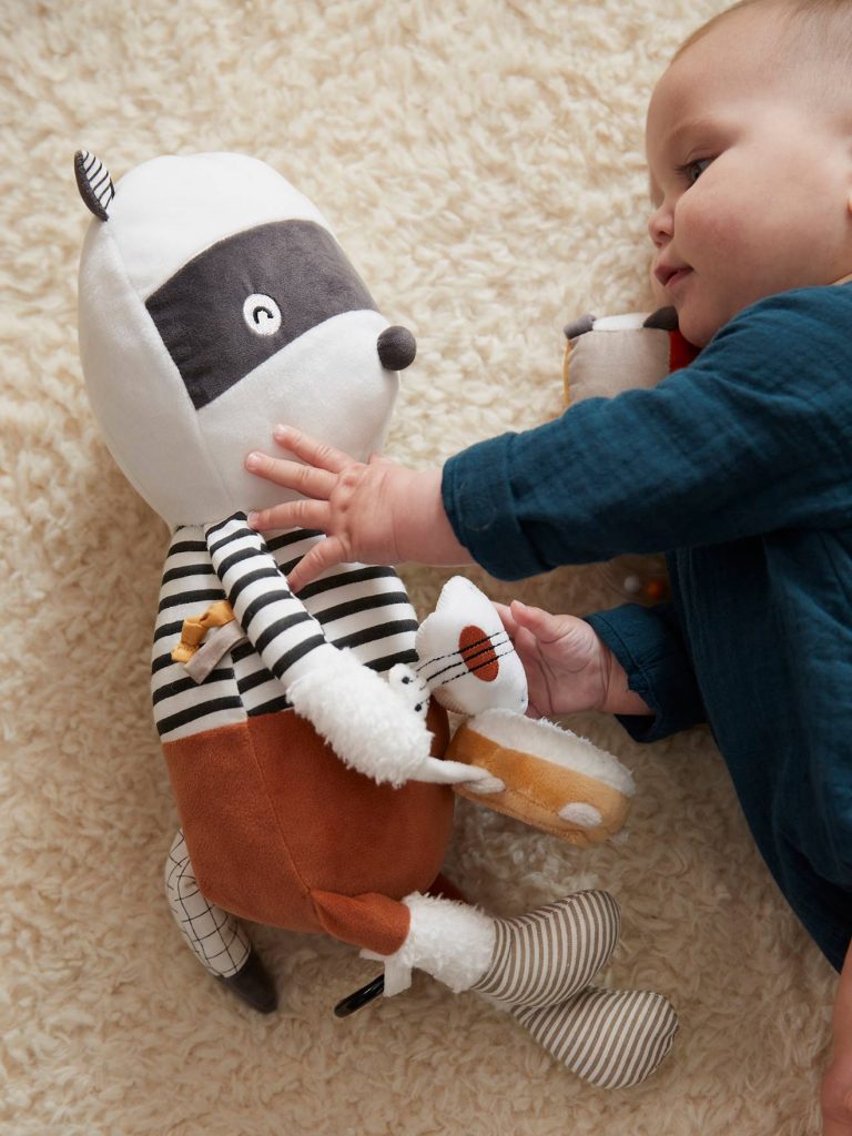 bébé joue avec une peluche raton laveur