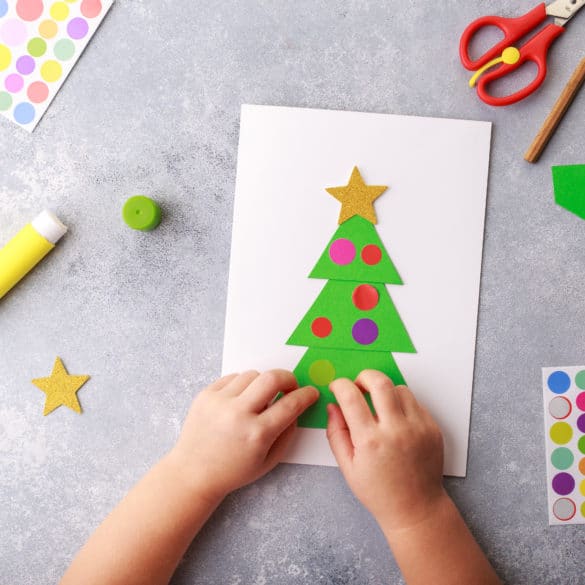 enfant fabrique une carte de noel sapin avec des gommettes