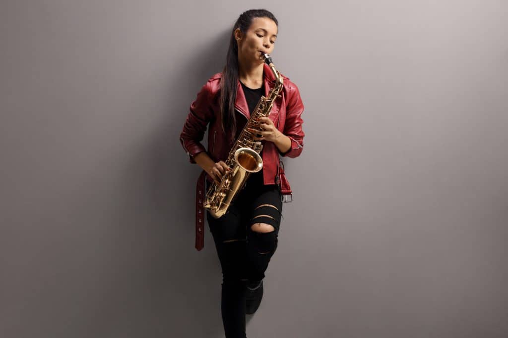 jeune femme joue du saxophone contre un mur