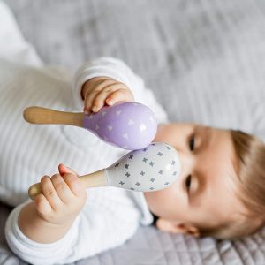 bébé allongé joue avec un maracas en bois