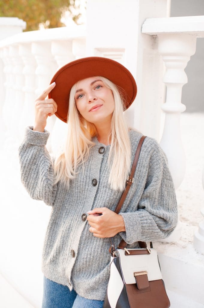 jeune femme cheveux longs blonds habillée avec un gilet gris et un chapeau rouge