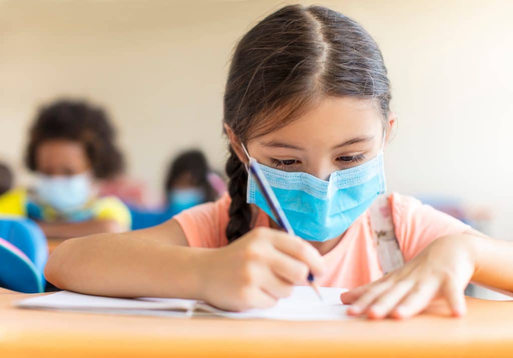 enfant écrit en classe et porte un masque covid