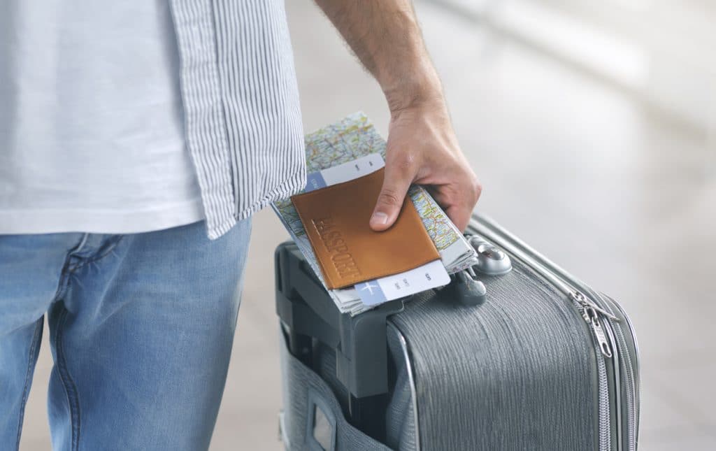 homme porte une valise avec passeport et billet à la main