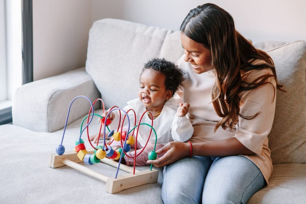 bébé et maman assis sur un canapé jouent avec un jeu d'eveil