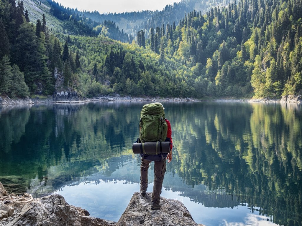 homme regarde un lac avec matériel de camping dans sac à dos