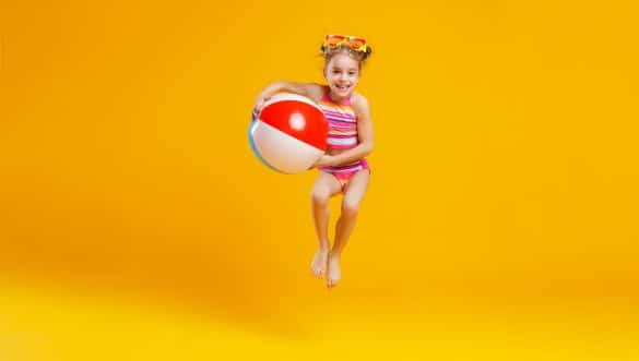 petite fille en maillot de bain 1 pièce court avec un ballon sous le bras