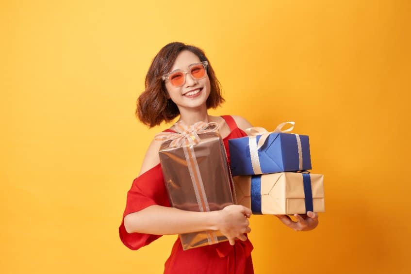 jeune femme asiatique avec lunette orange porte 3 cadeaux dans ses mains