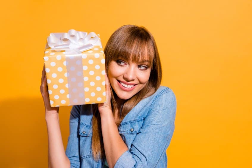 jeune femme cheveux longs tient un cadeau avec un ruban près de son visage