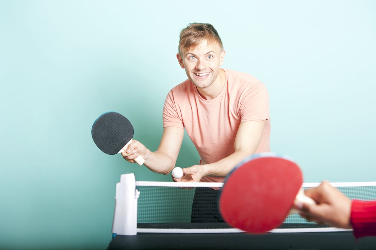 homme avec un tee shirt saumon tient une raquette de  ping pong dans sa main