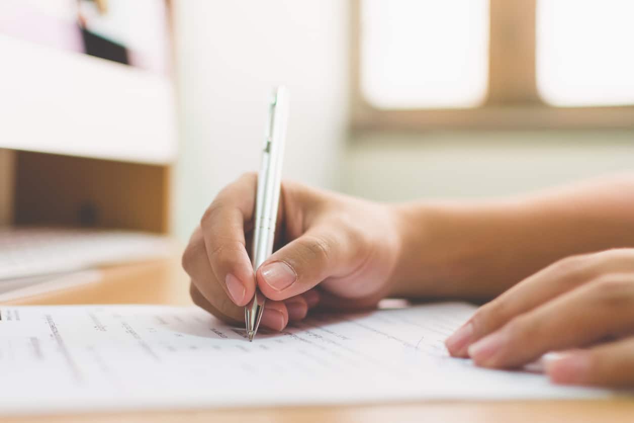 main avec un stylo blanc qui écrit sur une feuille