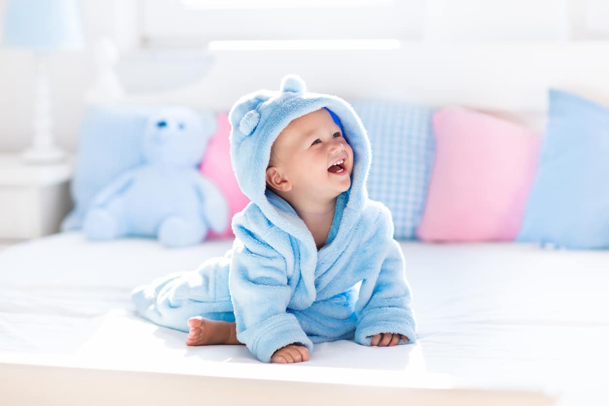 bébé habillé avec un peignoir de bain bleu assis sur un lit 