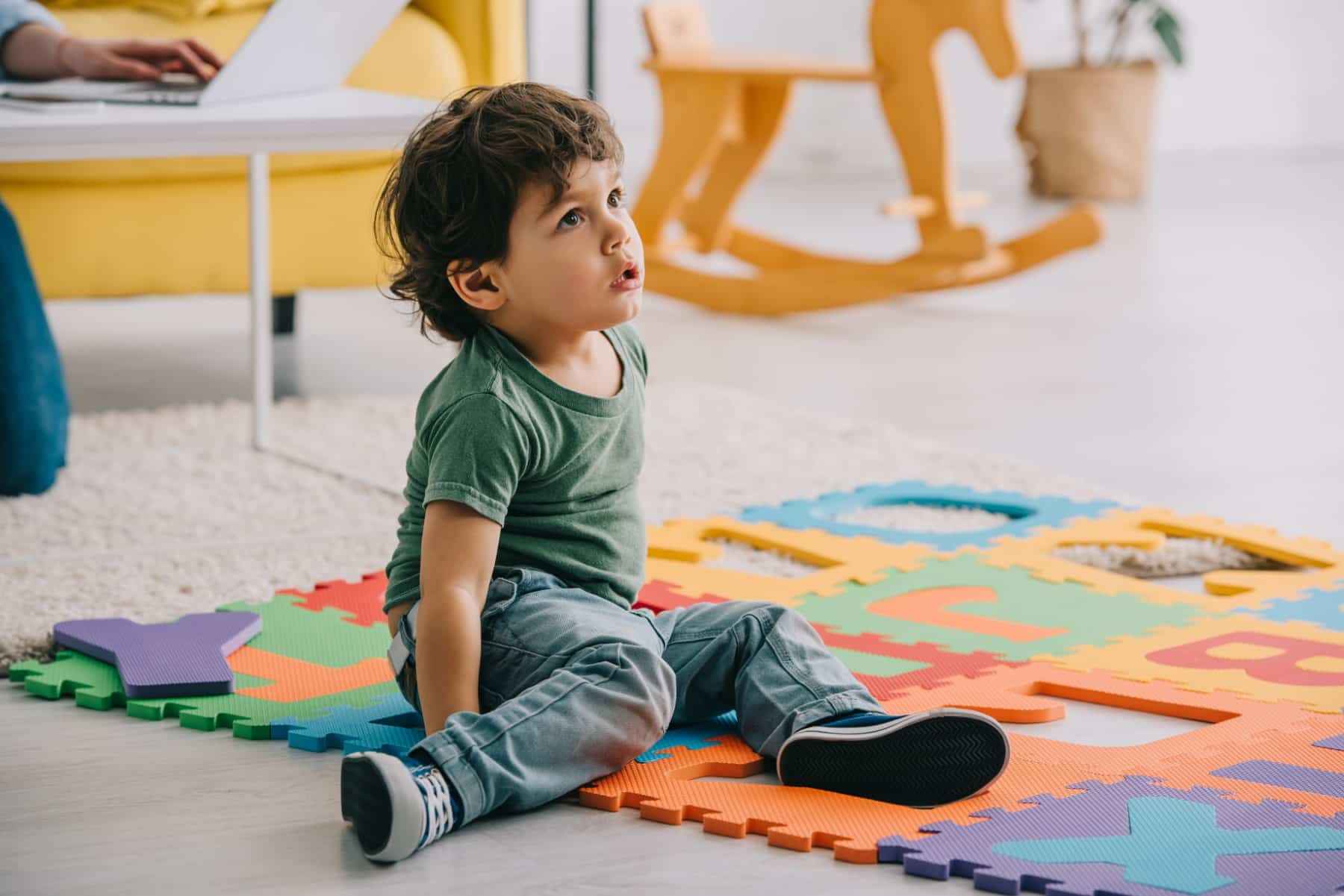 petit garçon qui porte un jean assis sur un tapis en mousse