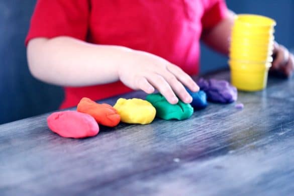 enfant appuie sur de la pâte à modeler de couleur rose, rouge, jaune, vert, bleu et violet