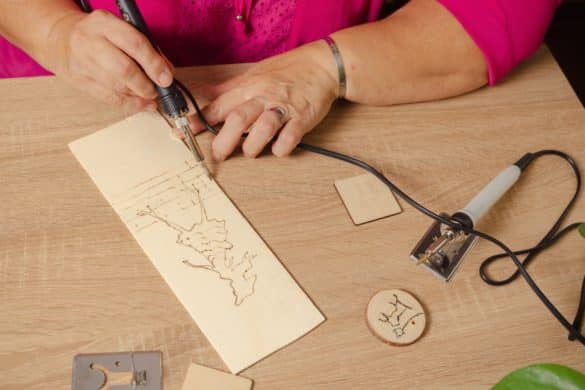 femme avec un tee shirt rouge dessine un modèle sur une planche en bois avec un pyrograveur