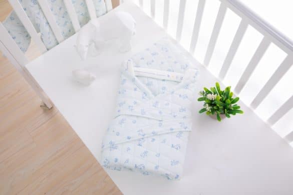 gigoteuse nid d'ange bébé bleu posée sur un lit bébé à barreaux