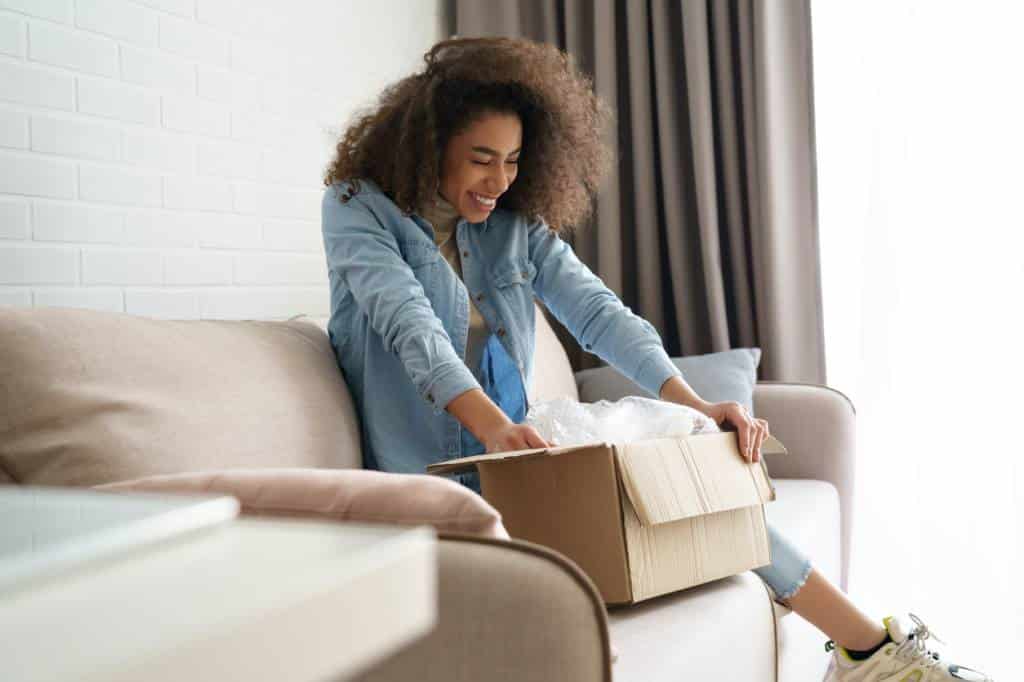 jeune femme assise sur un canapé ouvre un carton