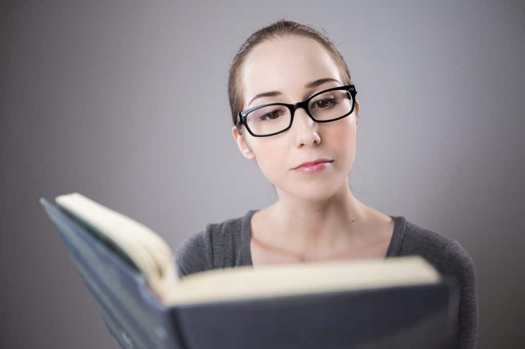 jeune femme avec lunettes lit un livre ouvert