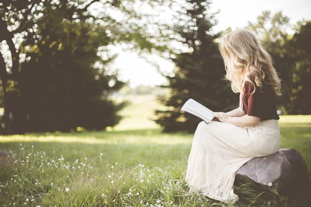 jeune femme blonde assise dans un champs lit un livre