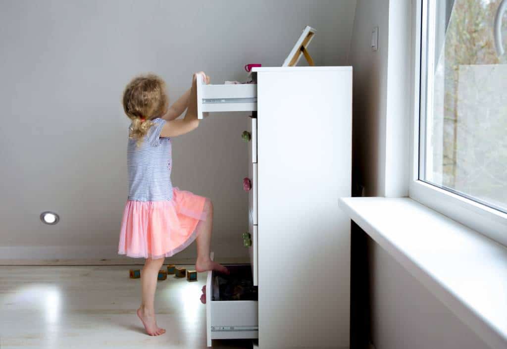 petite fille ouvre un tiroir de commode blanche